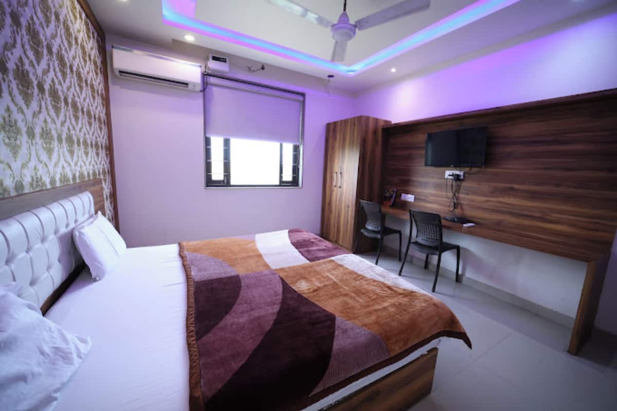 A bedroom with a bed, a desk, a chair, a television, and a ceiling fan.