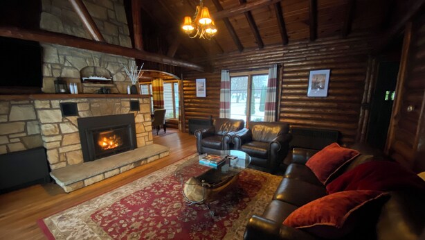 L’intérieur d’un chalet confortable, avec des murs en rondins de bois, une cheminée en pierre, des canapés en cuir et un lustre.