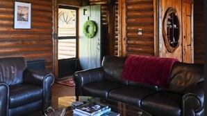 L’intérieur d’une cabane en rondins, avec un canapé en cuir, une table basse et un lustre.
