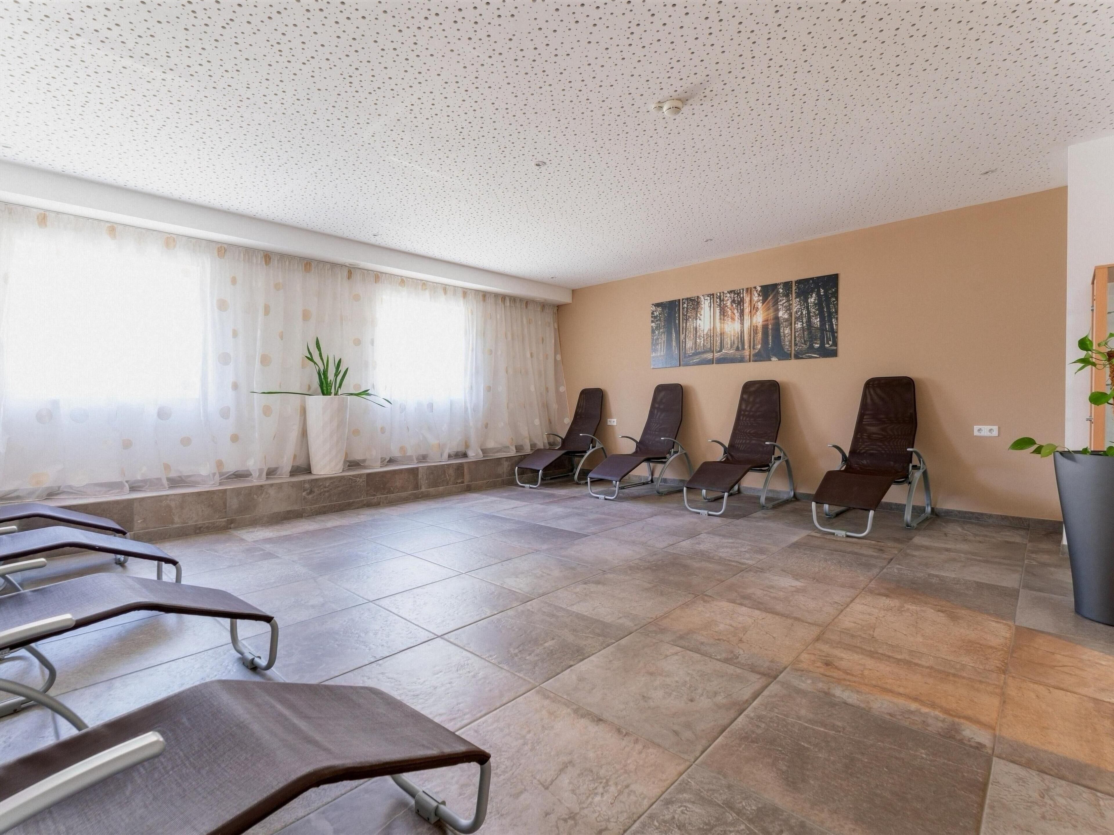 A waiting area with several reclining chairs, a large window with sheer curtains, and a wall-mounted artwork.
