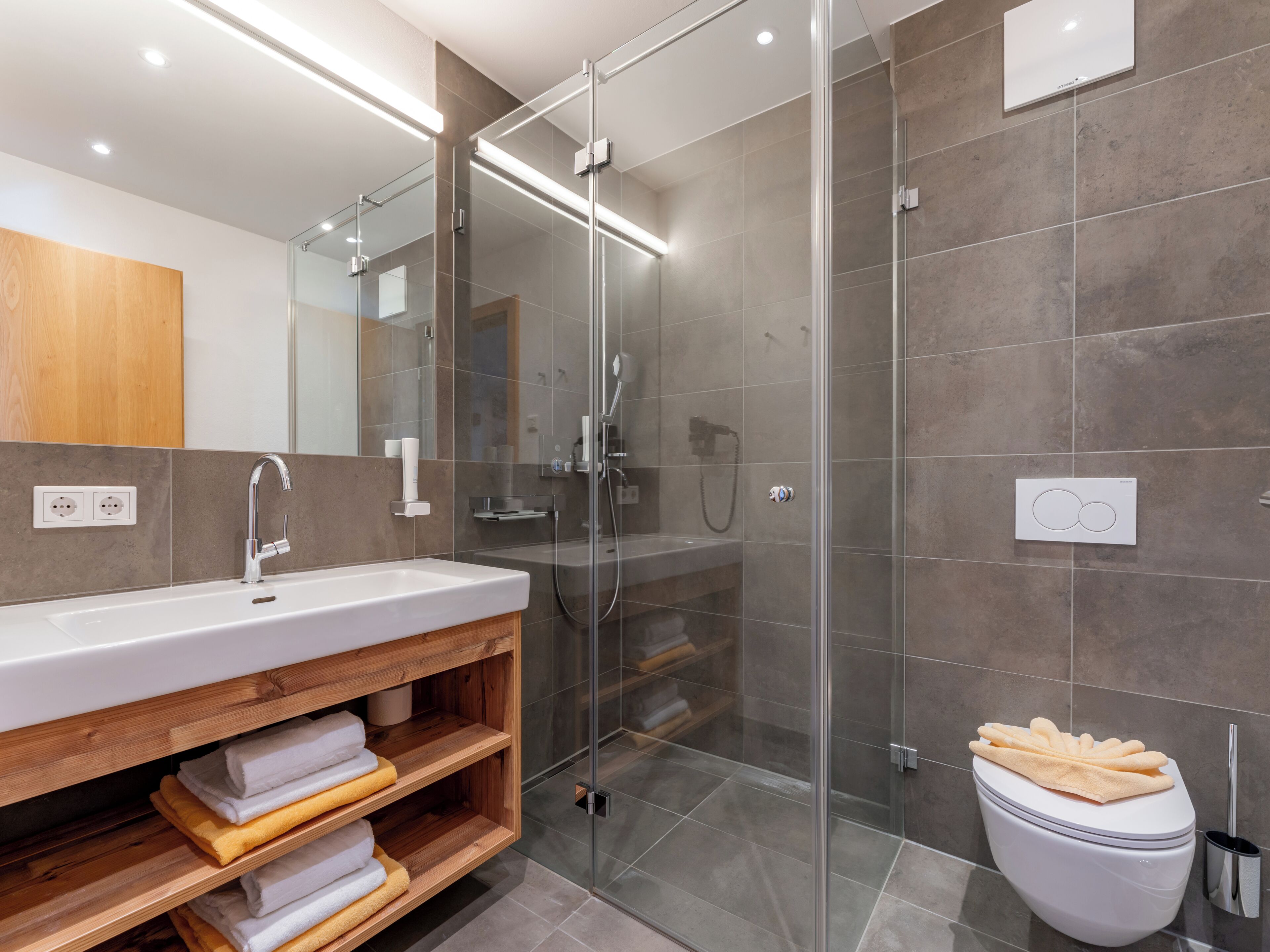 Et moderne badeværelse med et glasvægshus, et træbord med vask og toilet.