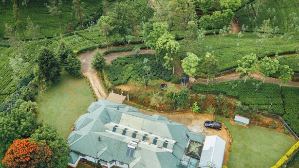 An aerial view of a property with terraced tea fields, a central building with a green roof, and a fenced yard. - Iona Bungalow by Lalan Leisure  (Hatton)