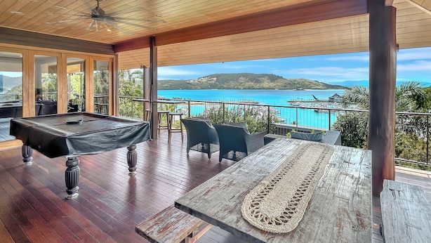 A wooden deck with a pool table, outdoor seating, and a view of a turquoise sea and distant hills. - The BoatHouse - Private 4 bedroom house (Whitsundays)