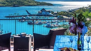 A seaside view with a marina, dining area with outdoor seating, and a mountain backdrop. - The BoatHouse - Private 4 bedroom house (Whitsundays)