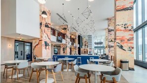 Um café moderno com mesas e cadeiras arredondadas, balcão azul e arte abstrata nas paredes.