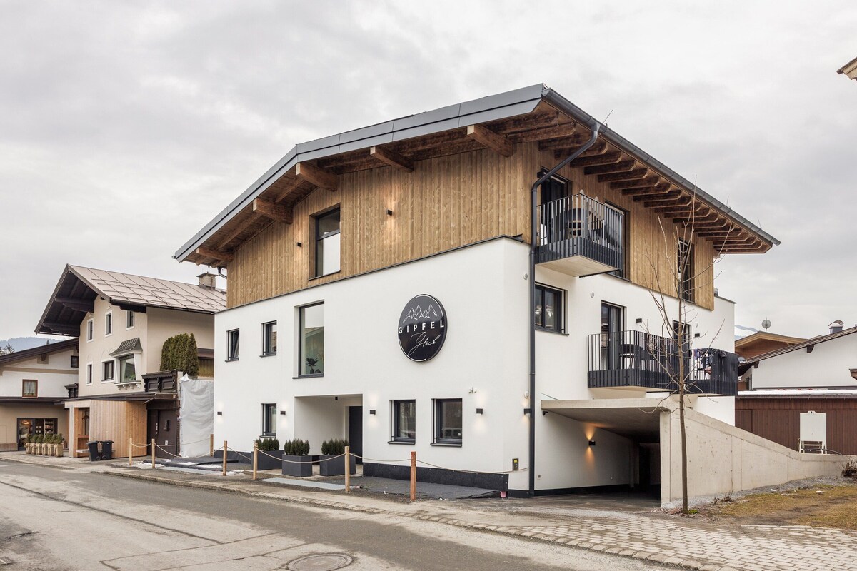A modern building with a wooden facade, a balcony, and a sign that reads 'GIPFEL Hotel'.