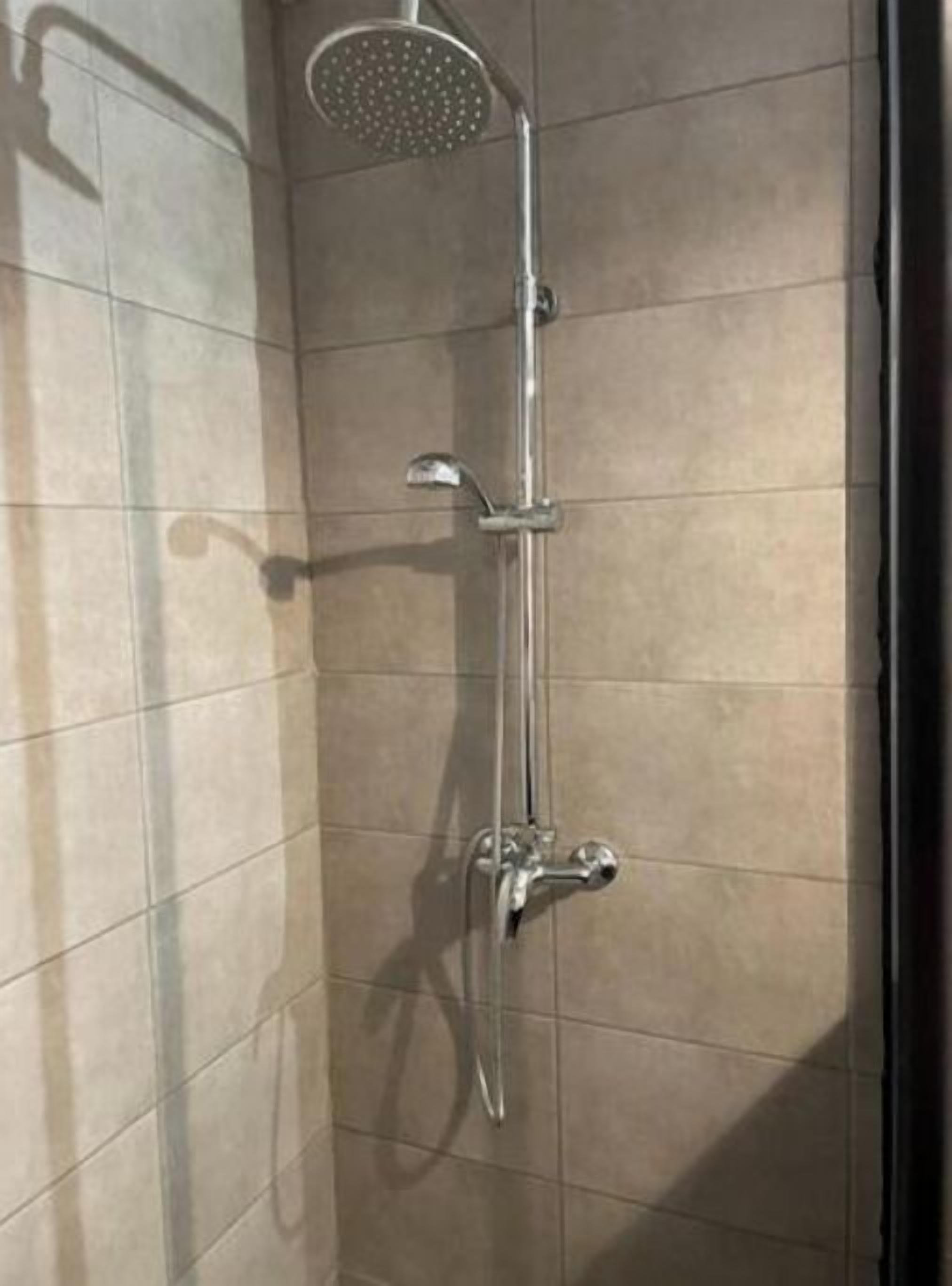 A shower with a handheld showerhead and a wall-mounted faucet.