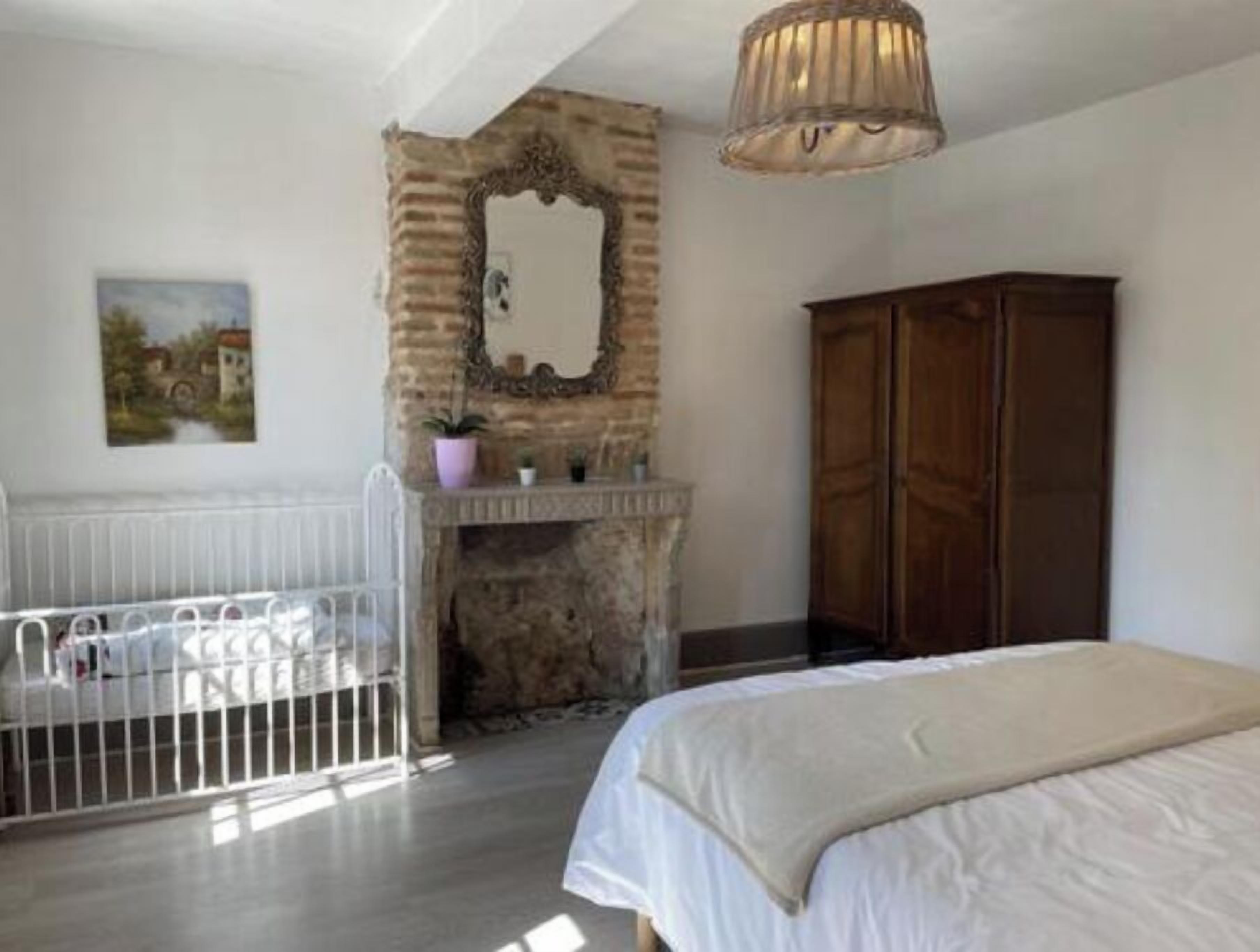 Una camera da letto con un letto bianco, un armadio in legno, un camino in pietra e un termosifone bianco.