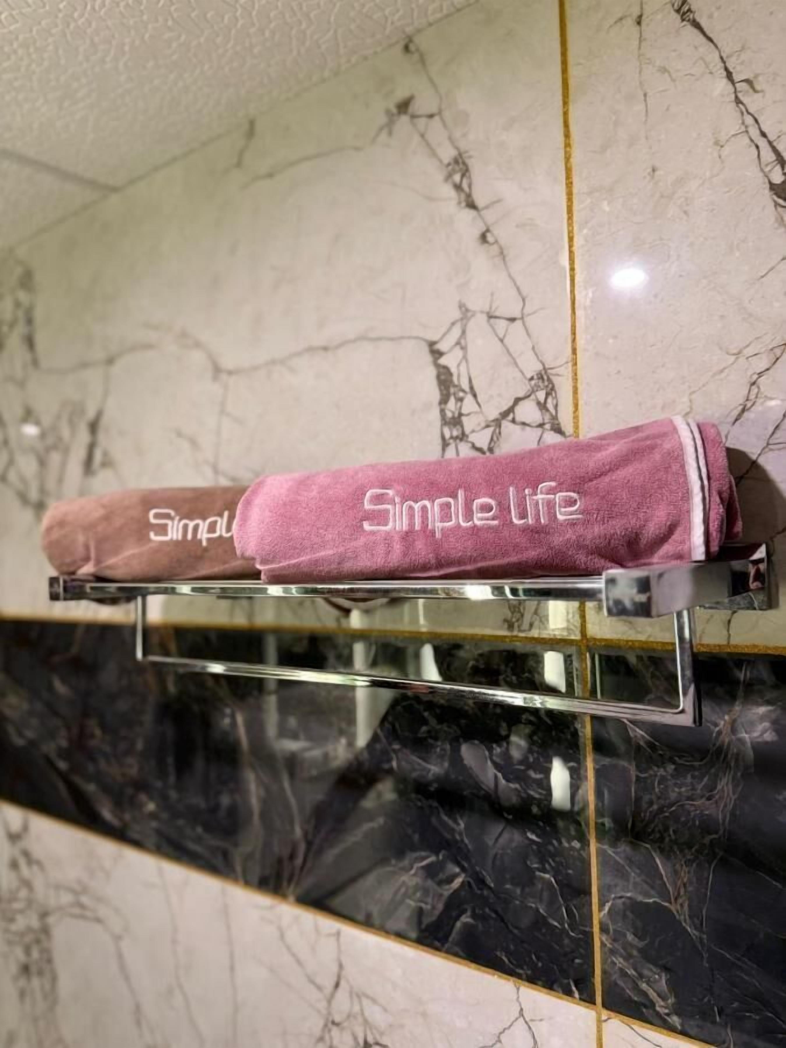 En handduksställning med två handdukar, en rosa och en brun, och på båda står texten ”Simple Life”.