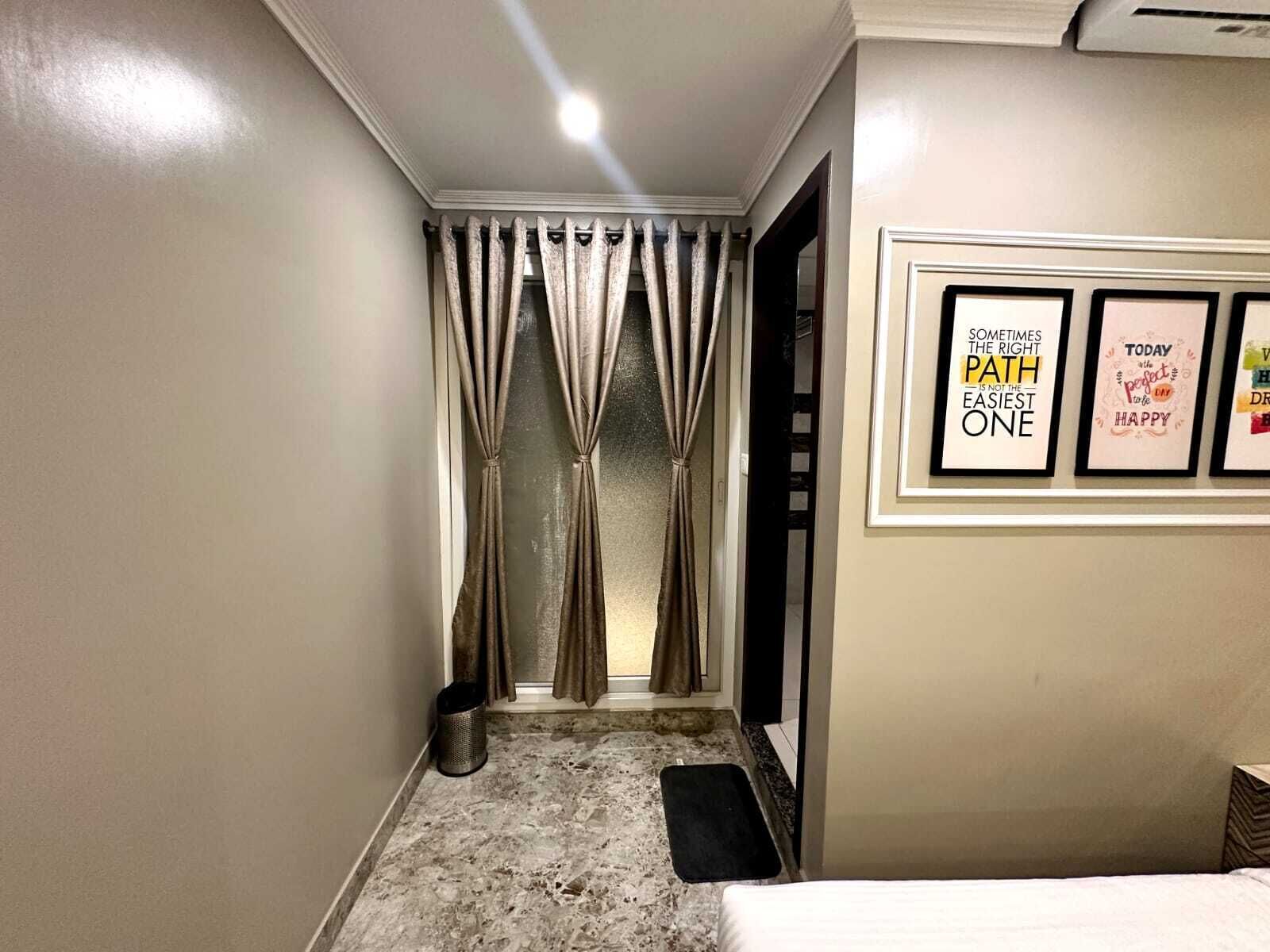 A narrow hallway with a door at the end, a trash bin, and a black mat on the floor.