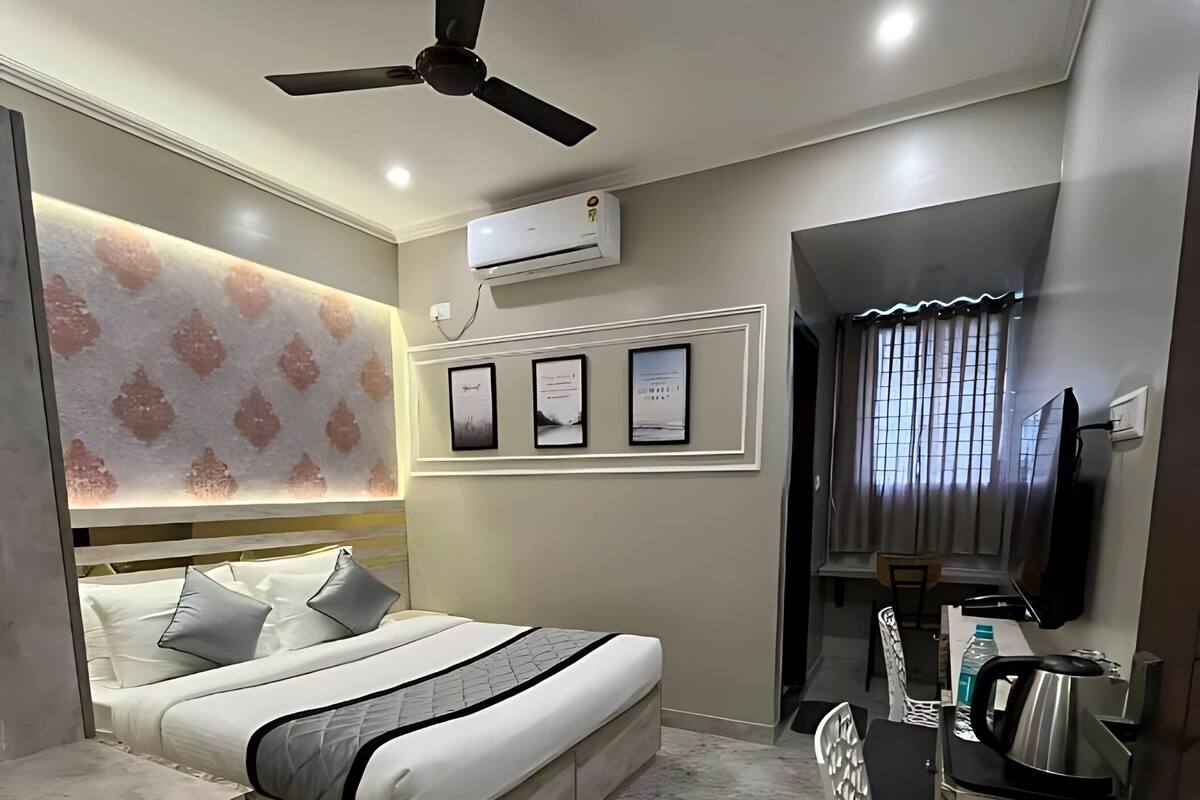 A modern hotel room with a bed, a desk with a kettle, a ceiling fan, and framed pictures on the wall.