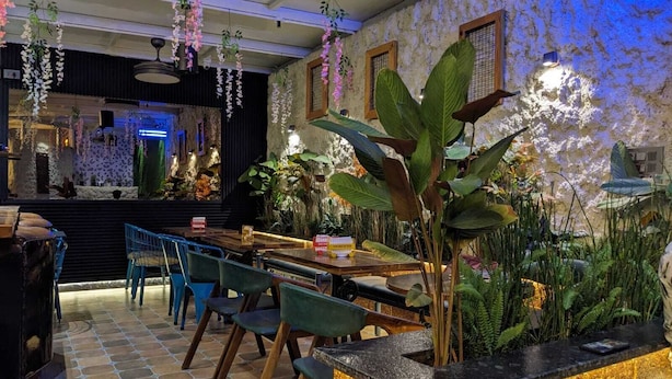 Een restaurant met een stenen muur, hangende orchideeën en diverse planten. Tafels en stoelen staan klaar voor het diner.