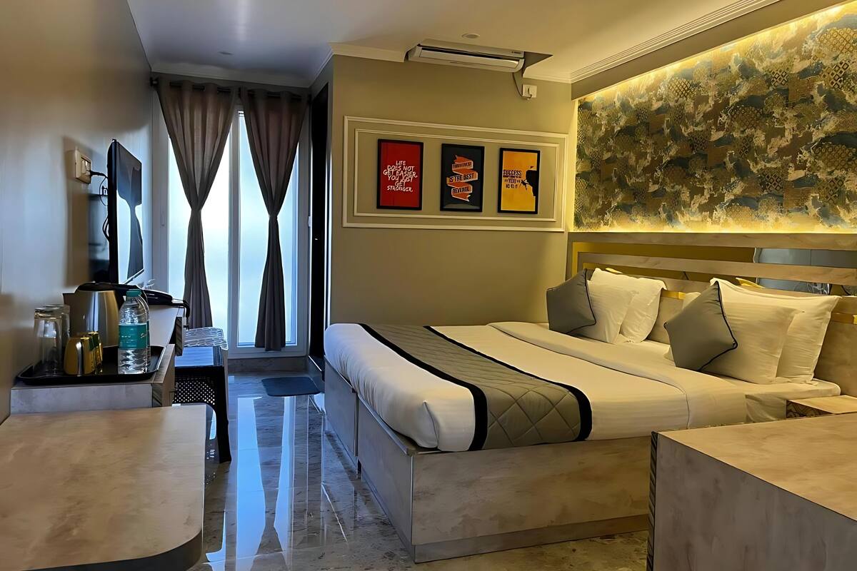 A hotel room with a bed, bedside tables, a desk with a chair, a TV, and a window with curtains.