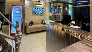Een moderne hotel lobby met een gebogen receptiebalie, een bank en een grote flatscreen televisie aan de muur.