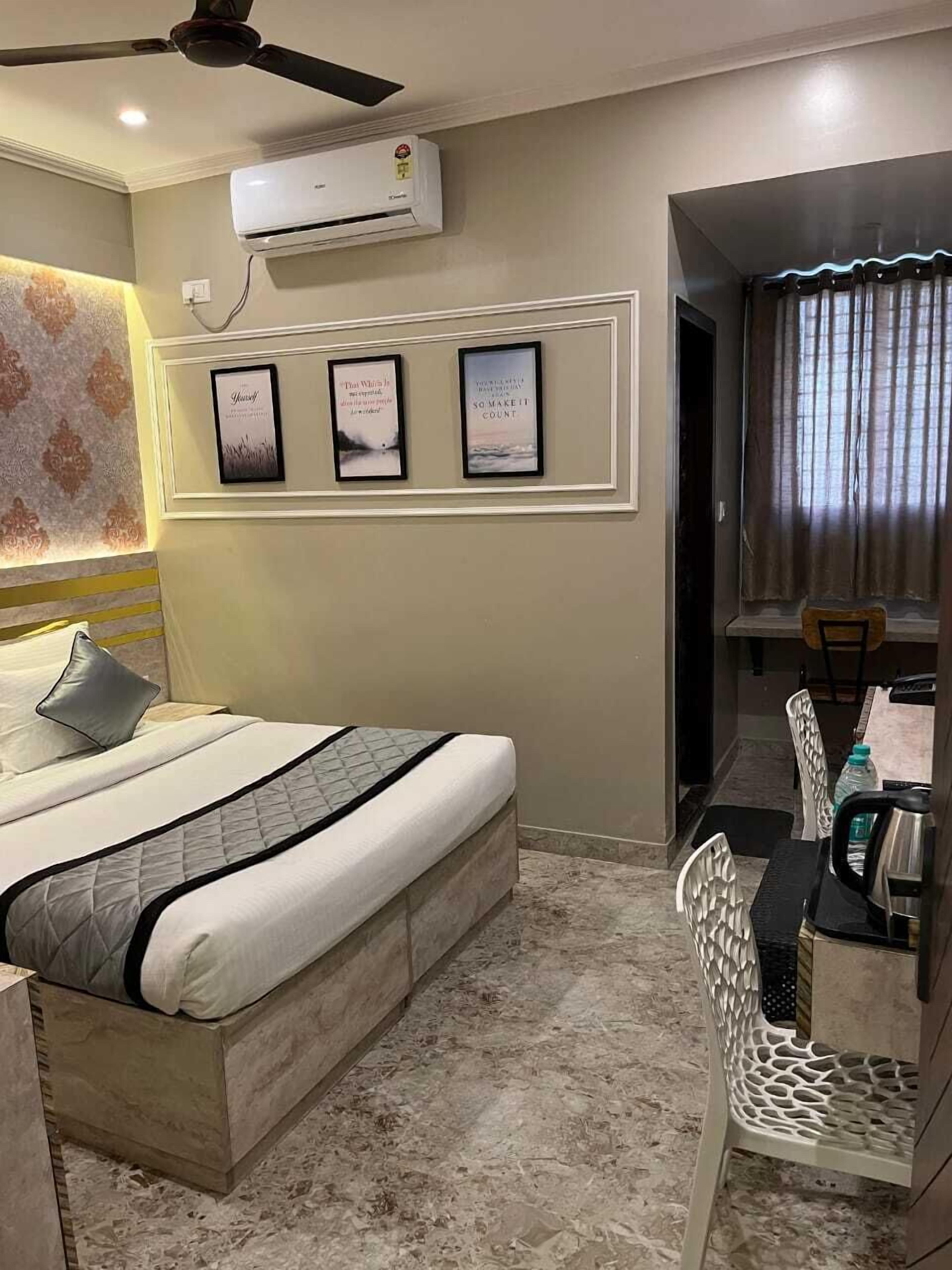 A hotel room with a bed, a dining table with chairs, an air conditioning unit, and framed inspirational quotes on the wall.