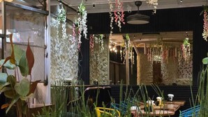 Een restaurantinterieur met bloemversieringen, een stenen muur en een zithoek met tafels en stoelen.