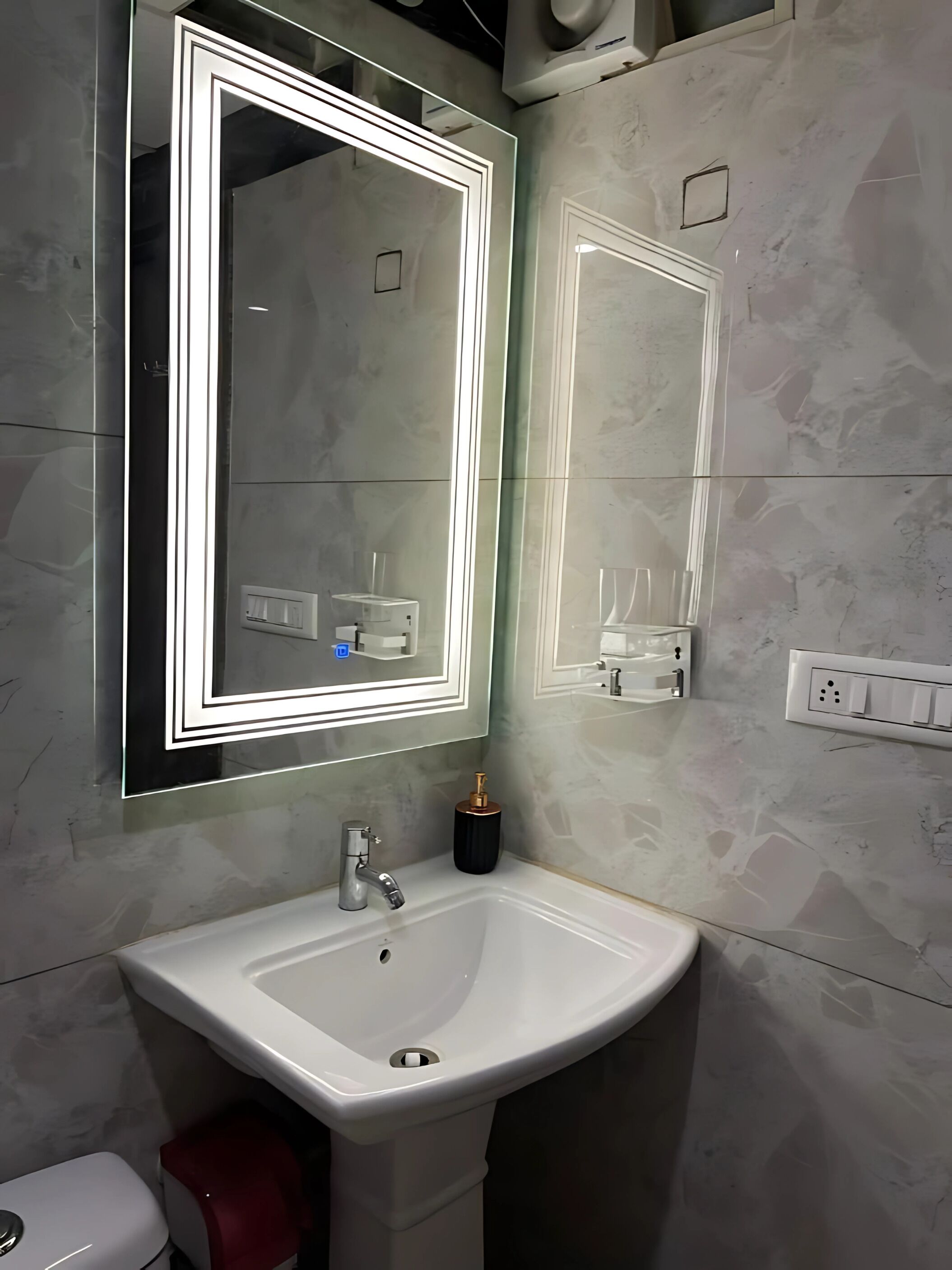 A bathroom with a white sink, a mirror with illuminated edges, and a wall-mounted light switch.