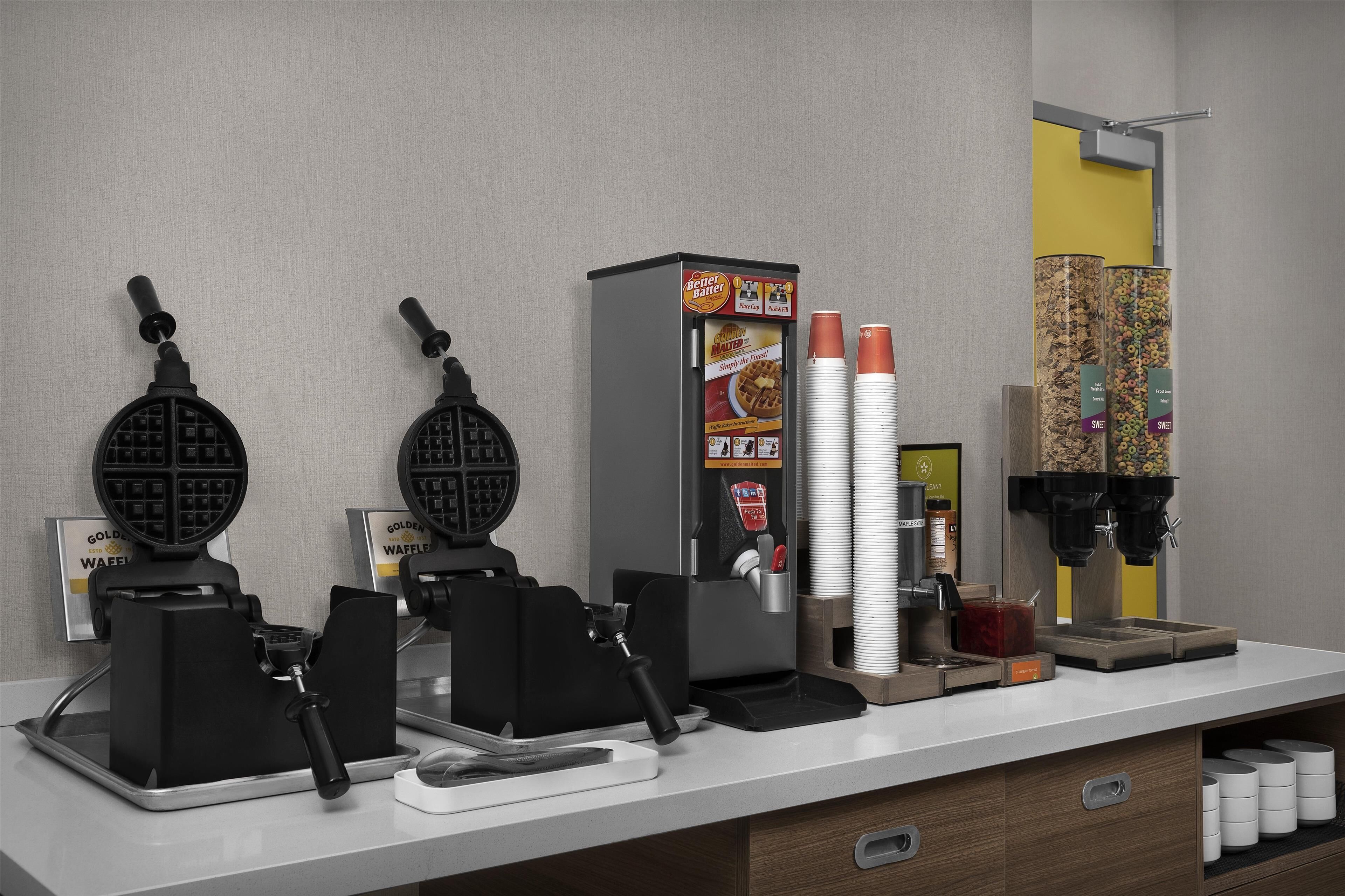 A breakfast bar with waffle makers, a waffle dispenser, and a coffee machine.
