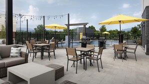 Un patio al aire libre con mesas y sillas, sombrillas amarillas, una piscina y una parrilla.