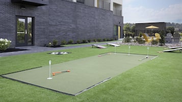A modern building with a brick facade, a flat roof, and a small patio area with artificial grass and outdoor furniture.