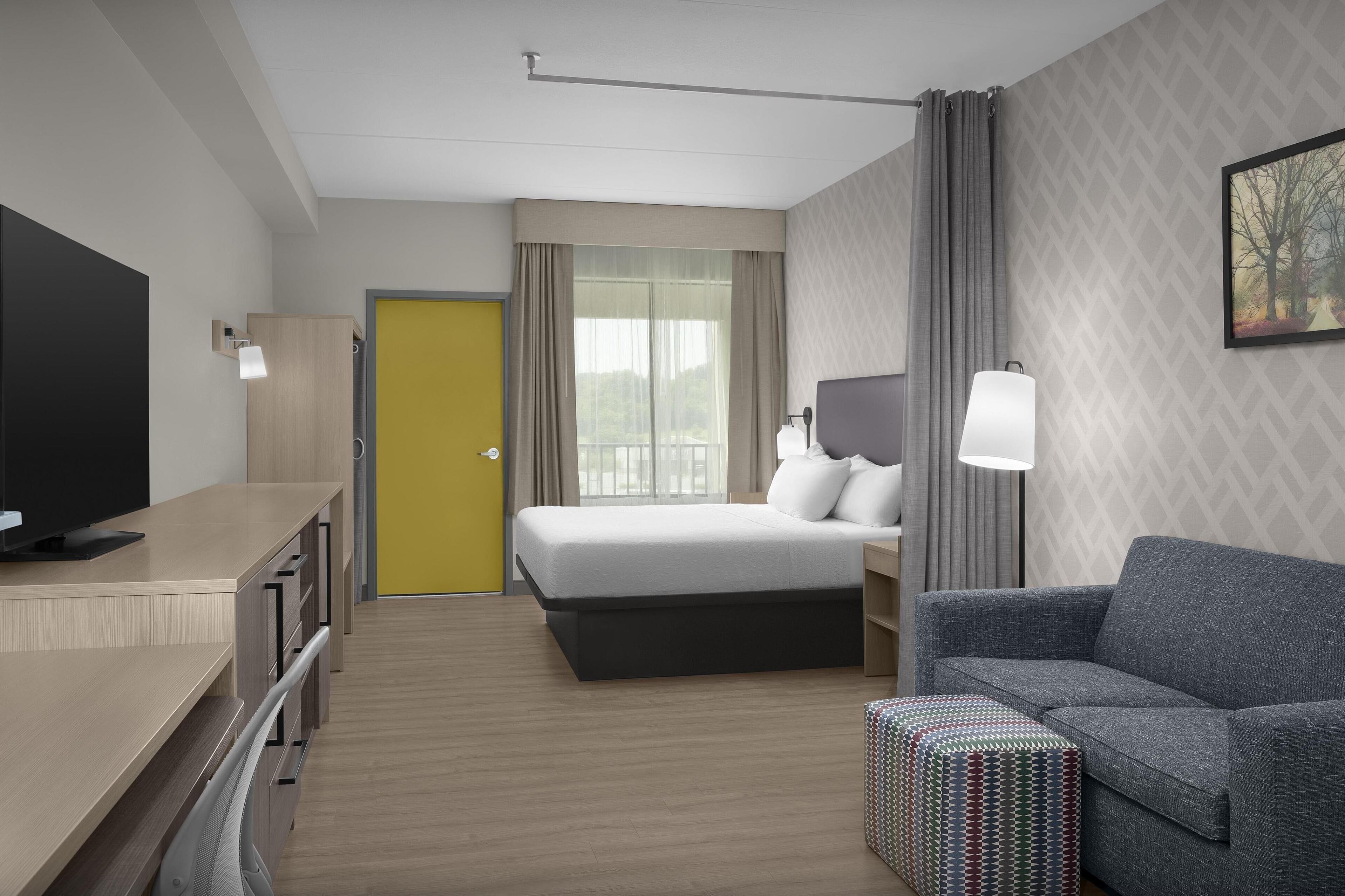 A modern hotel room with a bed, a desk with a TV, a sofa, and a patterned wall.