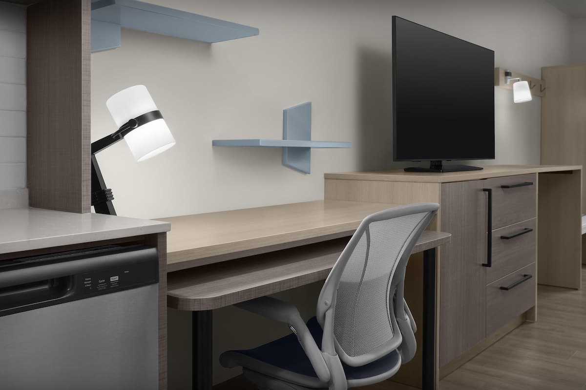 A modern kitchen with a dishwasher, a sink, a chair, a TV, and a cabinet.
