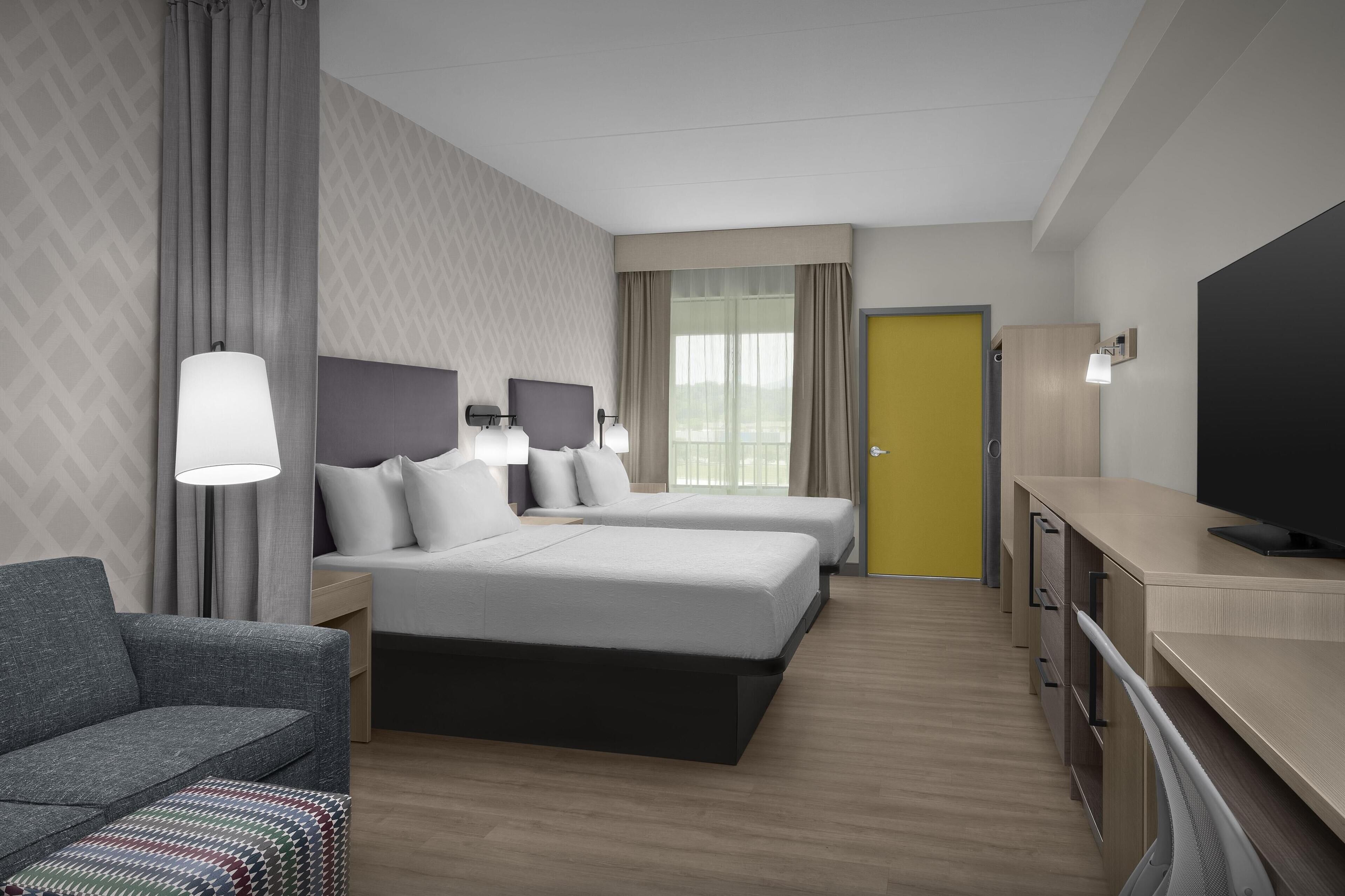 Habitación de hotel con dos camas, un sofá, un escritorio y televisión, y un baño.