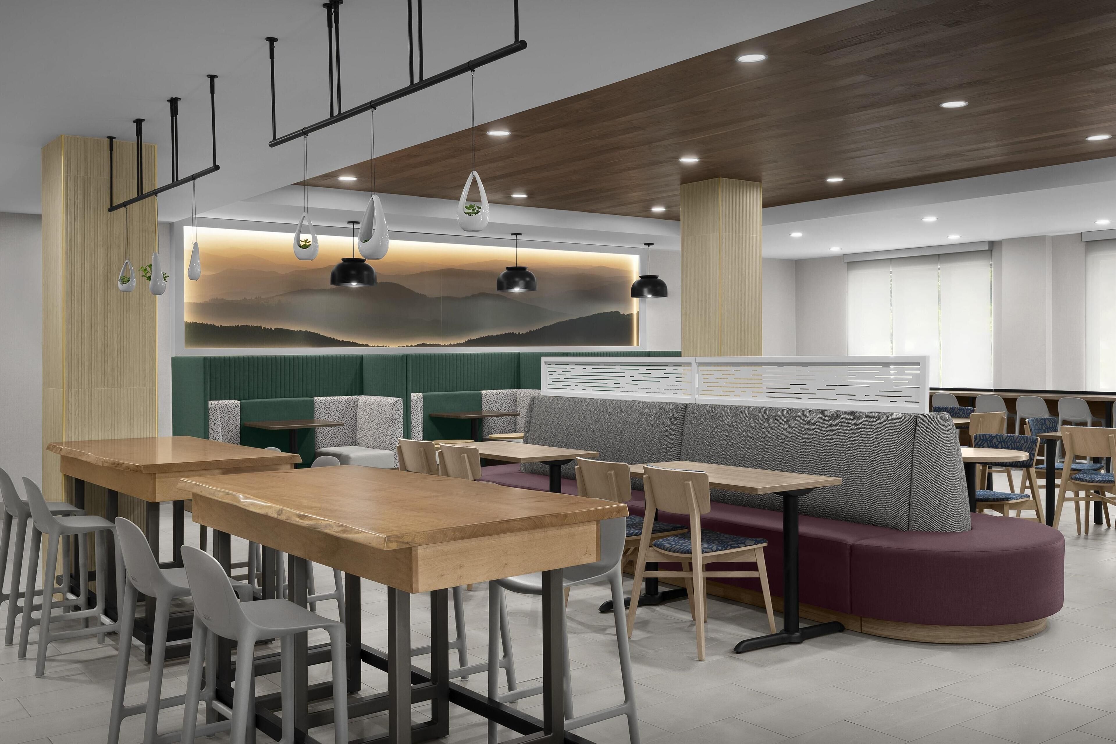 A modern restaurant with wooden tables, grey chairs, and a green booth area.