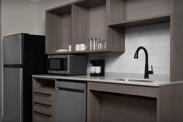 Cocina compacta equipada con refrigerador, microondas, cafetera y pileta con grifo negro.