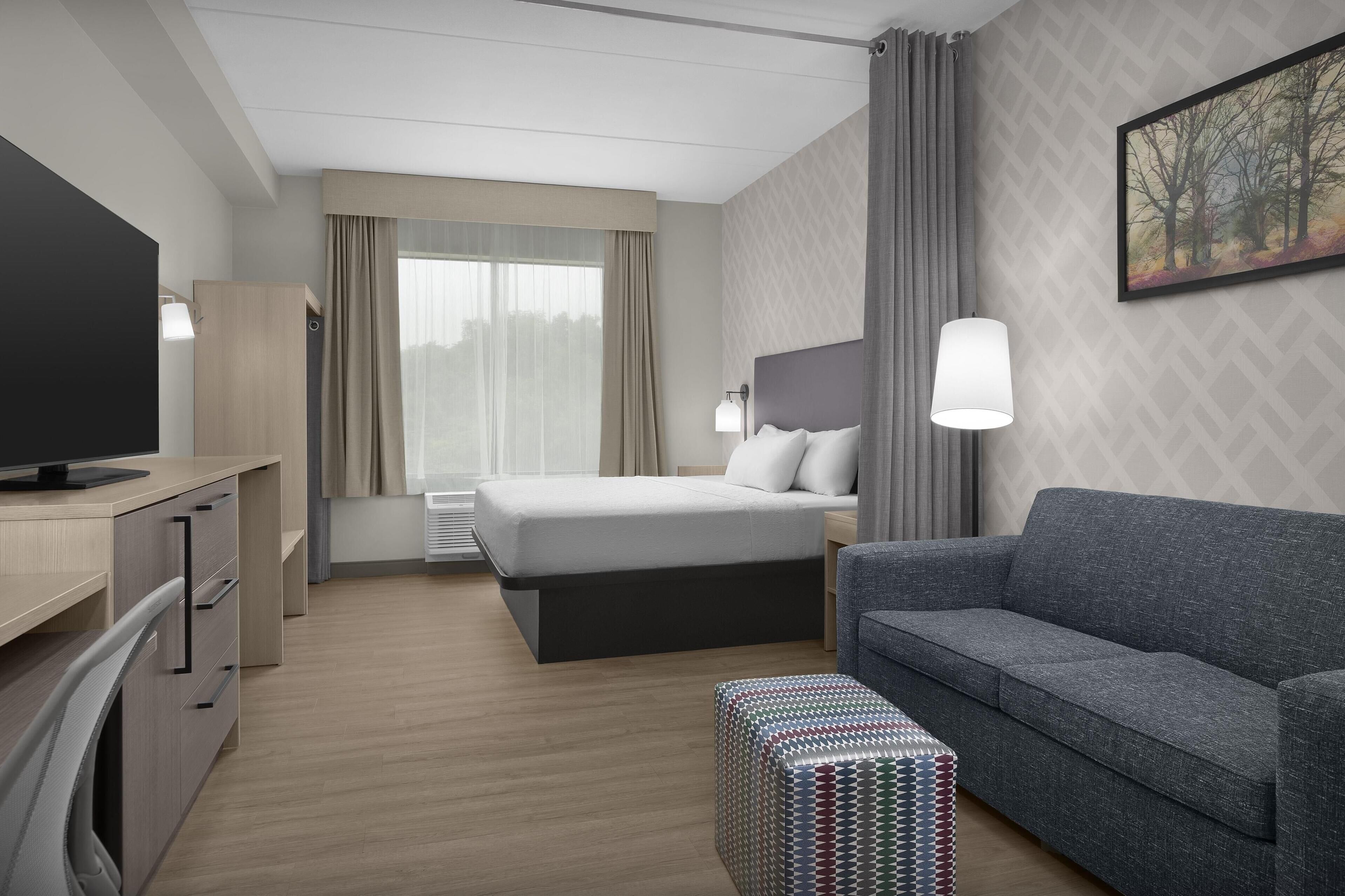 Una habitación de hotel con cama, sofá, televisión, escritorio y pared con diseño.
