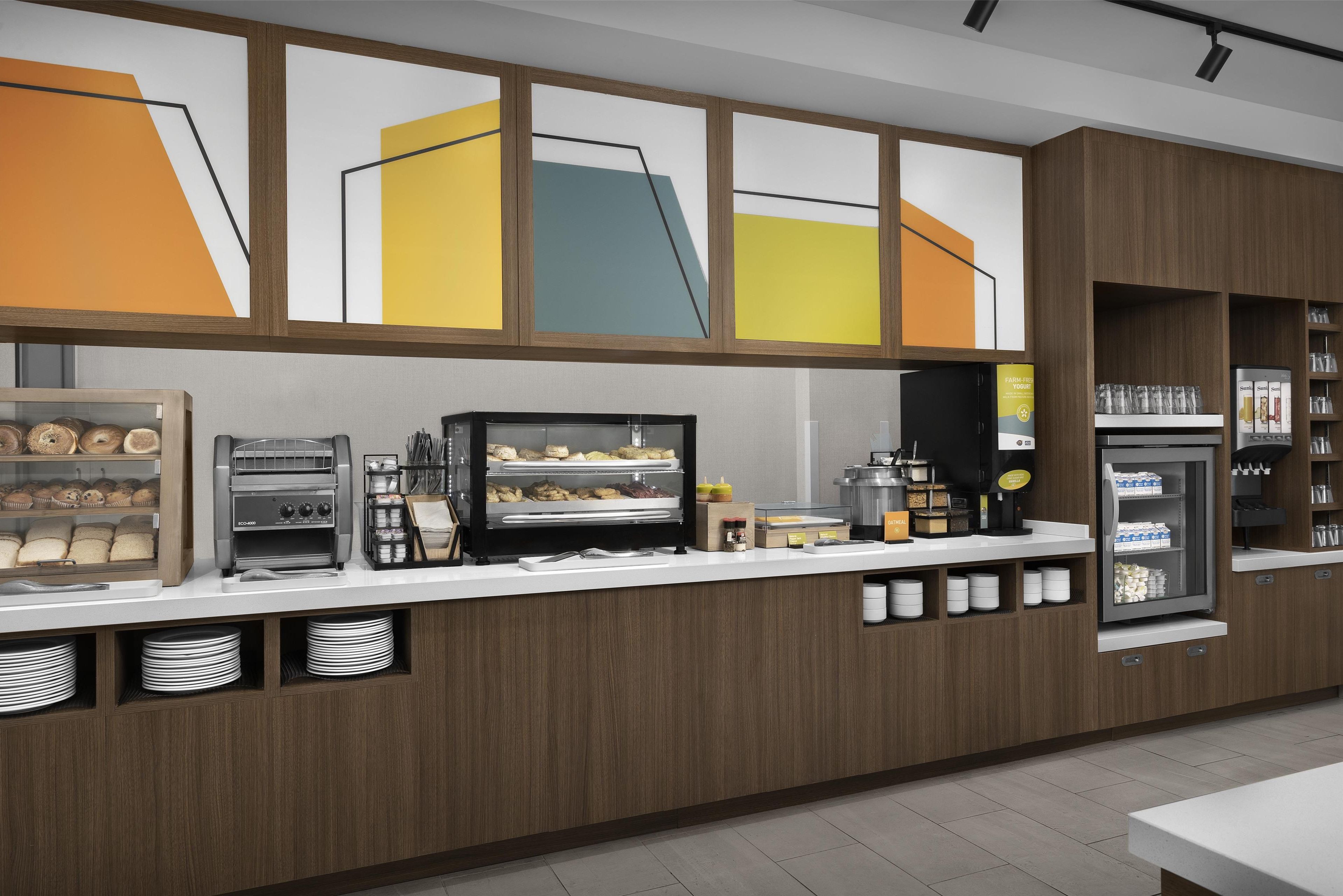 A modern breakfast bar with a coffee machine, toaster, and display case with pastries.