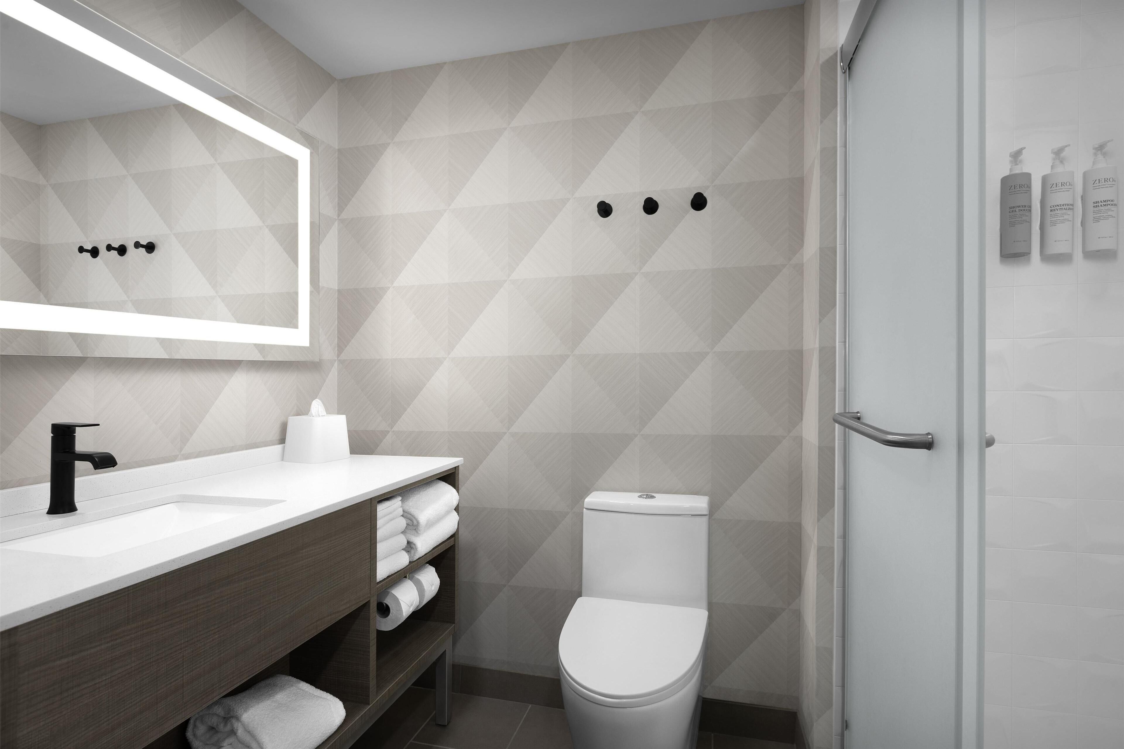 A modern bathroom with a white sink, dark wooden vanity, a toilet, and a glass shower enclosure.