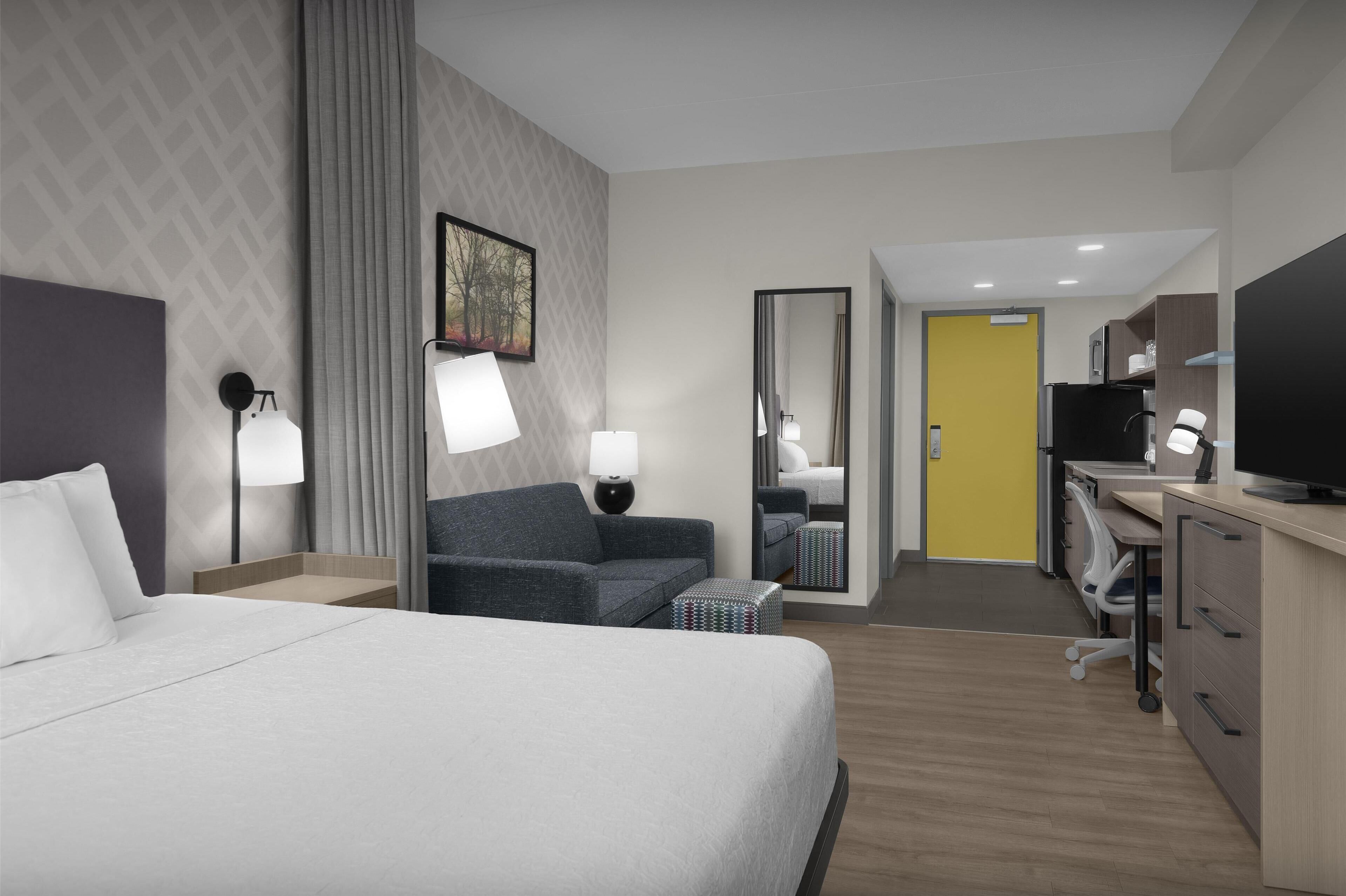 Una camera d'albergo con un letto, una scrivania, una sedia, una televisione e uno specchio.