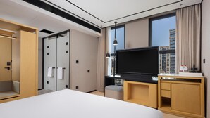 Habitación de hotel con cama, televisión, escritorio, armario y ventana con vistas a la ciudad.