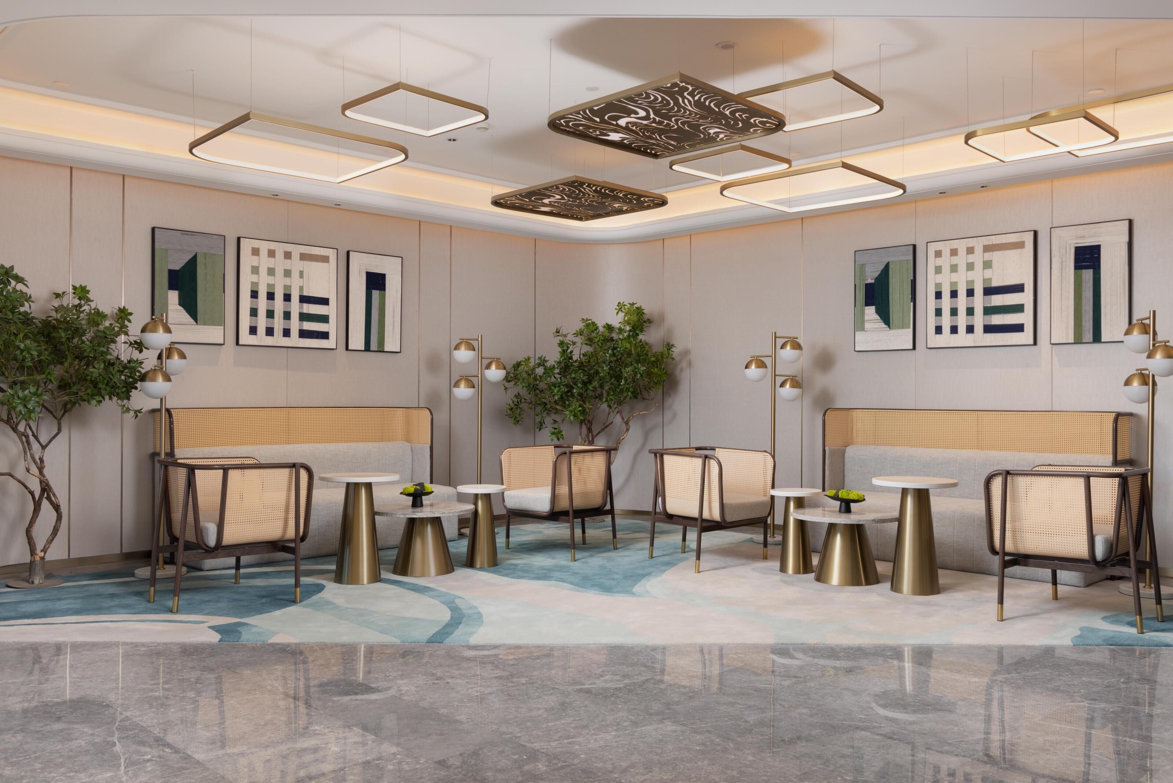 A modern hotel lobby with a seating area, decorative ceiling lights, and wall art.