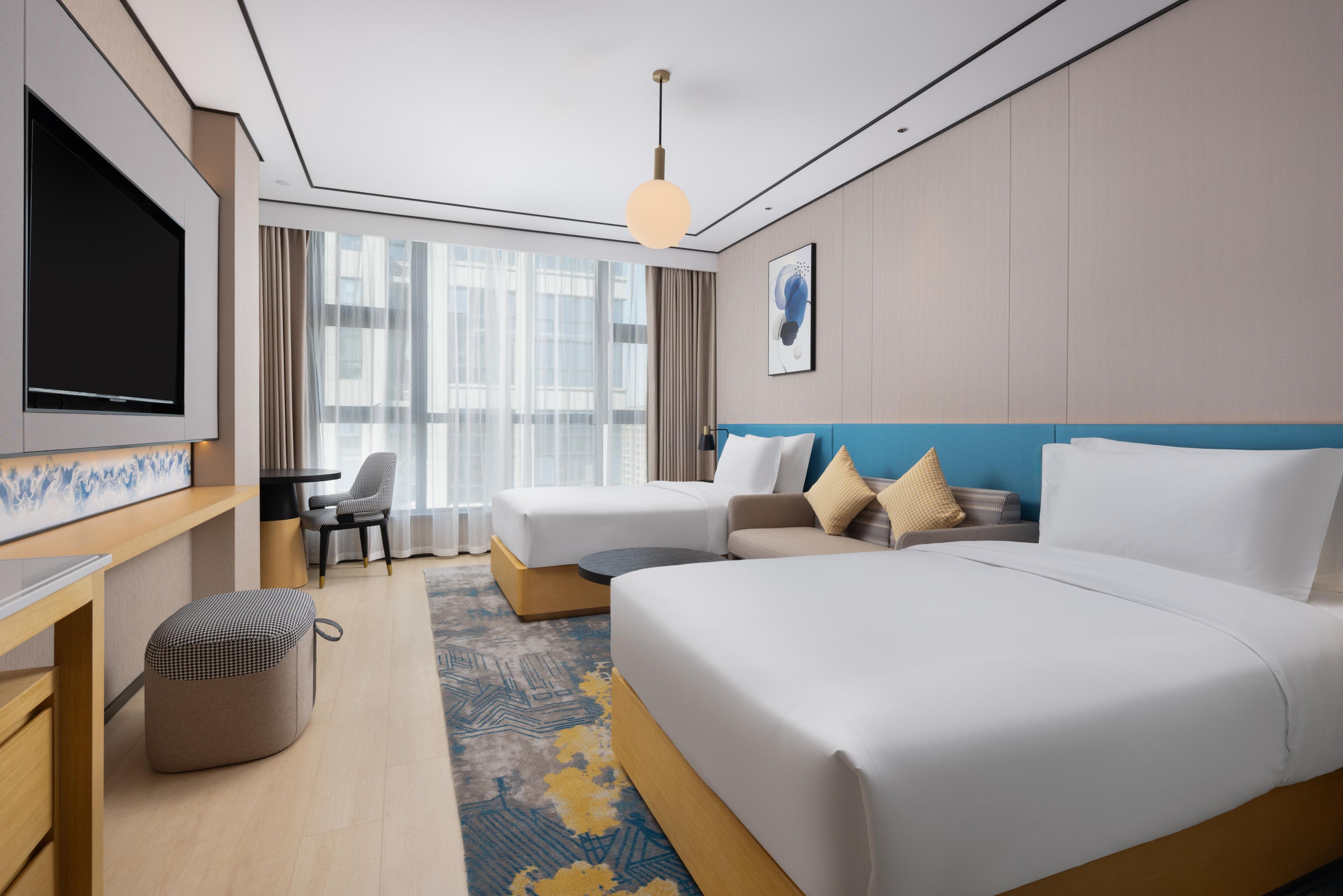 A hotel room with a bed, a desk, a chair, a TV, and a window with curtains.