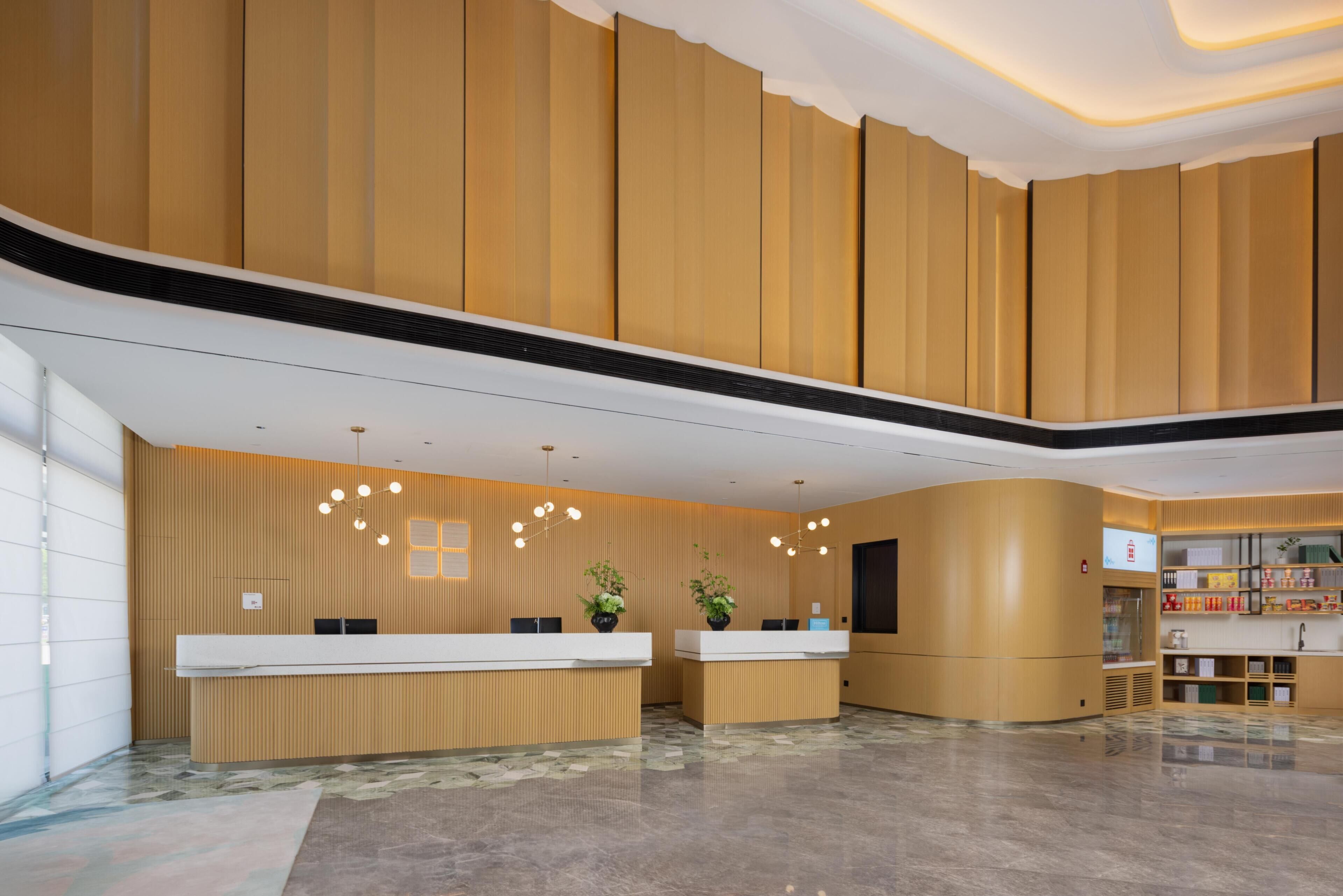 Un área de recepción con un mostrador curvo, dos plantas en macetas y un aplique de pared.