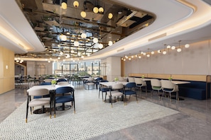 Un restaurant moderne avec un plafond haut, des conduits apparents et un mélange de tables rondes et rectangulaires.