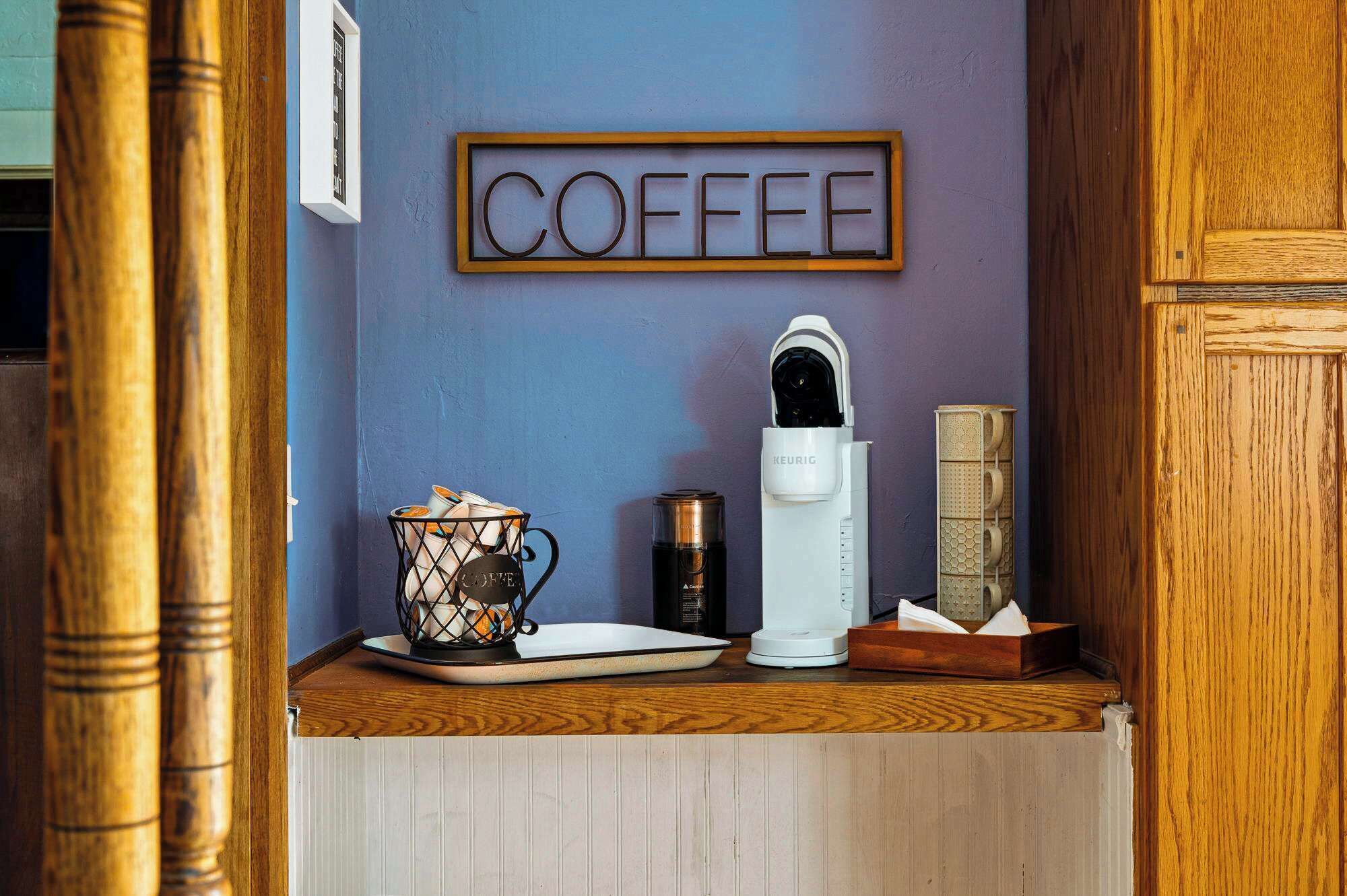 Un coin café équipé d’une machine à café Keurig, d’une tasse à café et d’une affiche sur le thème du café accrochée au mur.