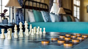 Un échiquier avec les pièces disposées sur une table, dans une pièce où se trouvent un lit et des rideaux.
