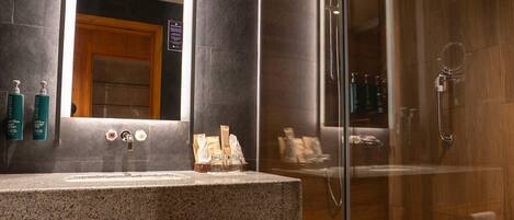 A modern bathroom with a granite countertop, a glass shower enclosure, and wooden cabinetry.