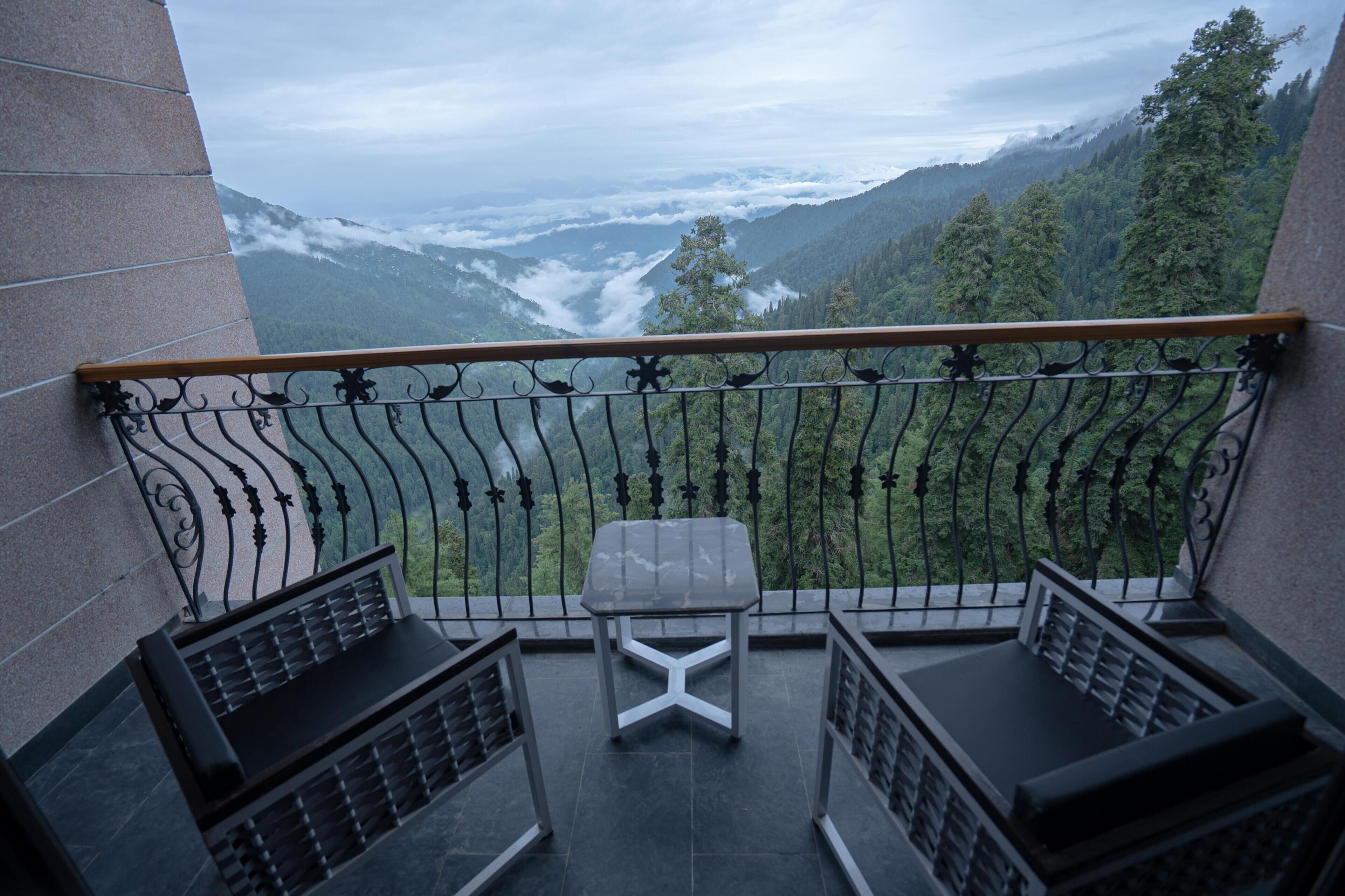 Un balcón con vistas a un paisaje montañoso, dos sillas y una mesita.