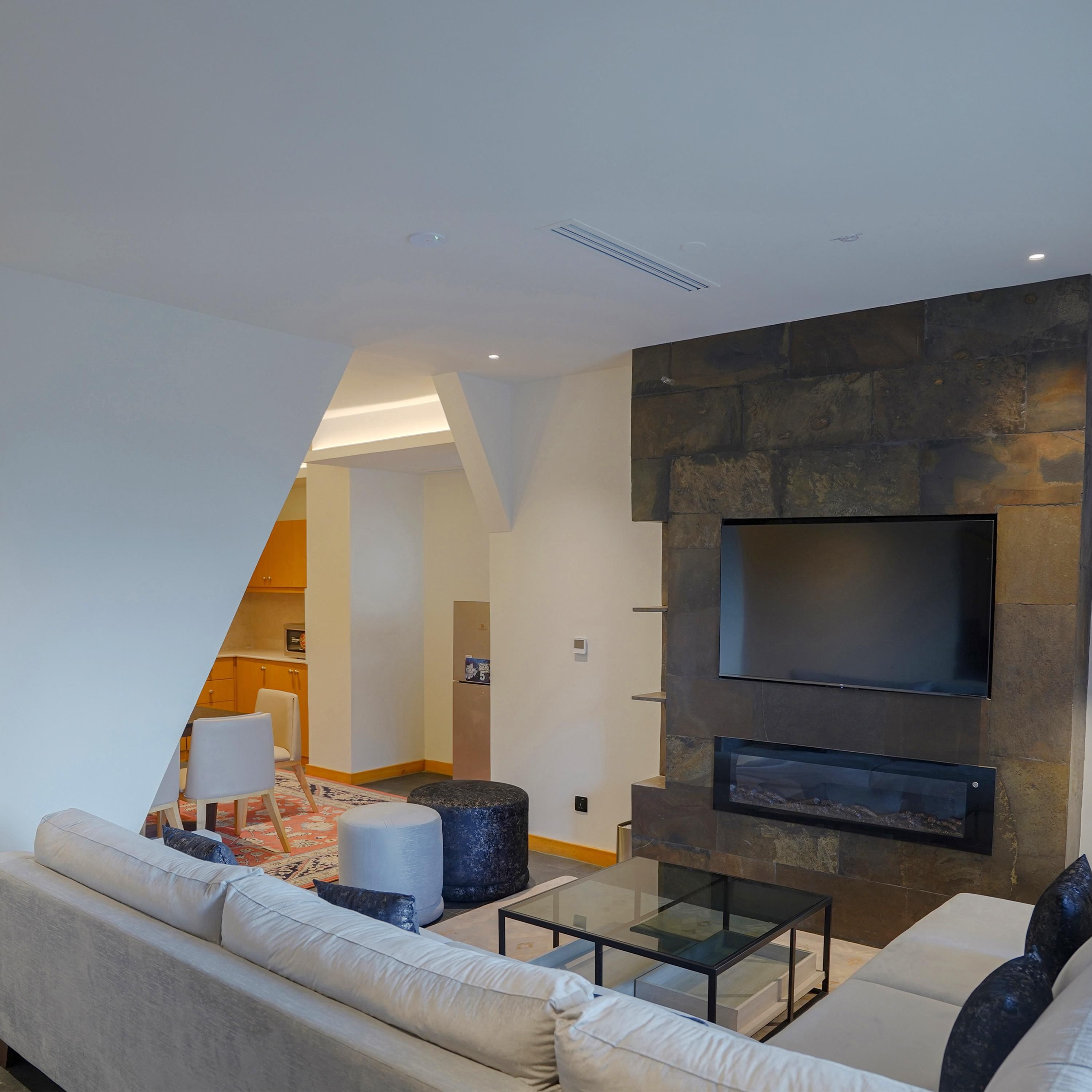 A modern living room with a sofa, a glass coffee table, and a flat-screen TV mounted on a stone wall.