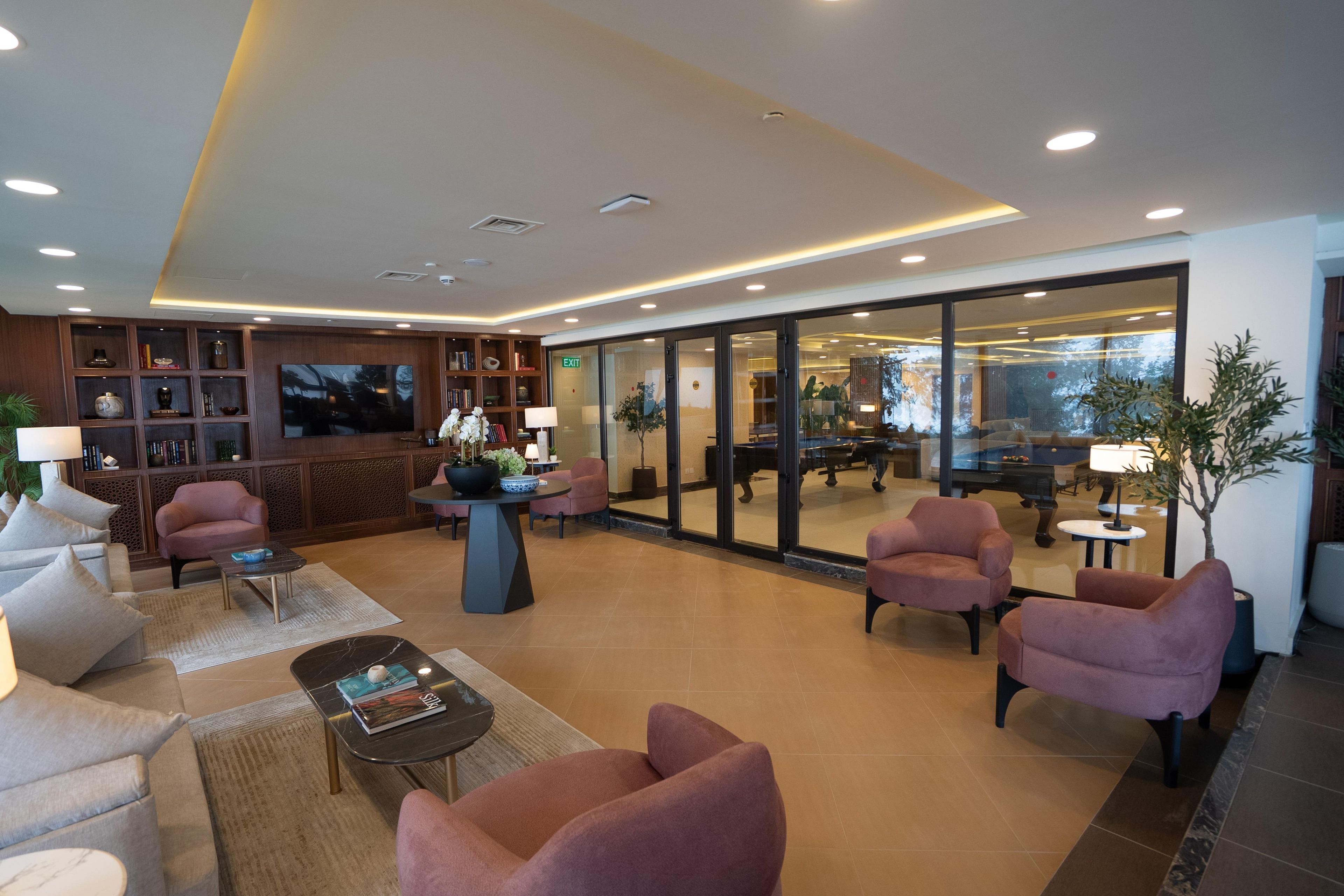 A modern lobby with seating, a television, and a glass wall leading to a dining area.