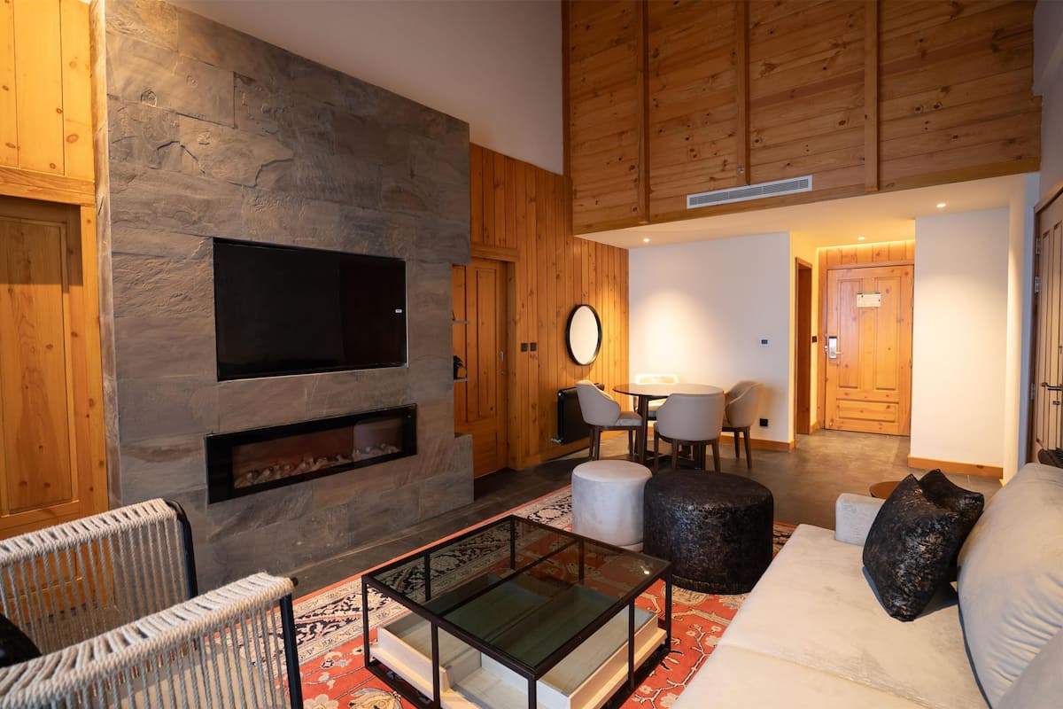 Een moderne woonkamer met een stenen muur, houten plafond, een flatscreen televisie, een open haard en een gezellige zithoek met een bank en een poef.