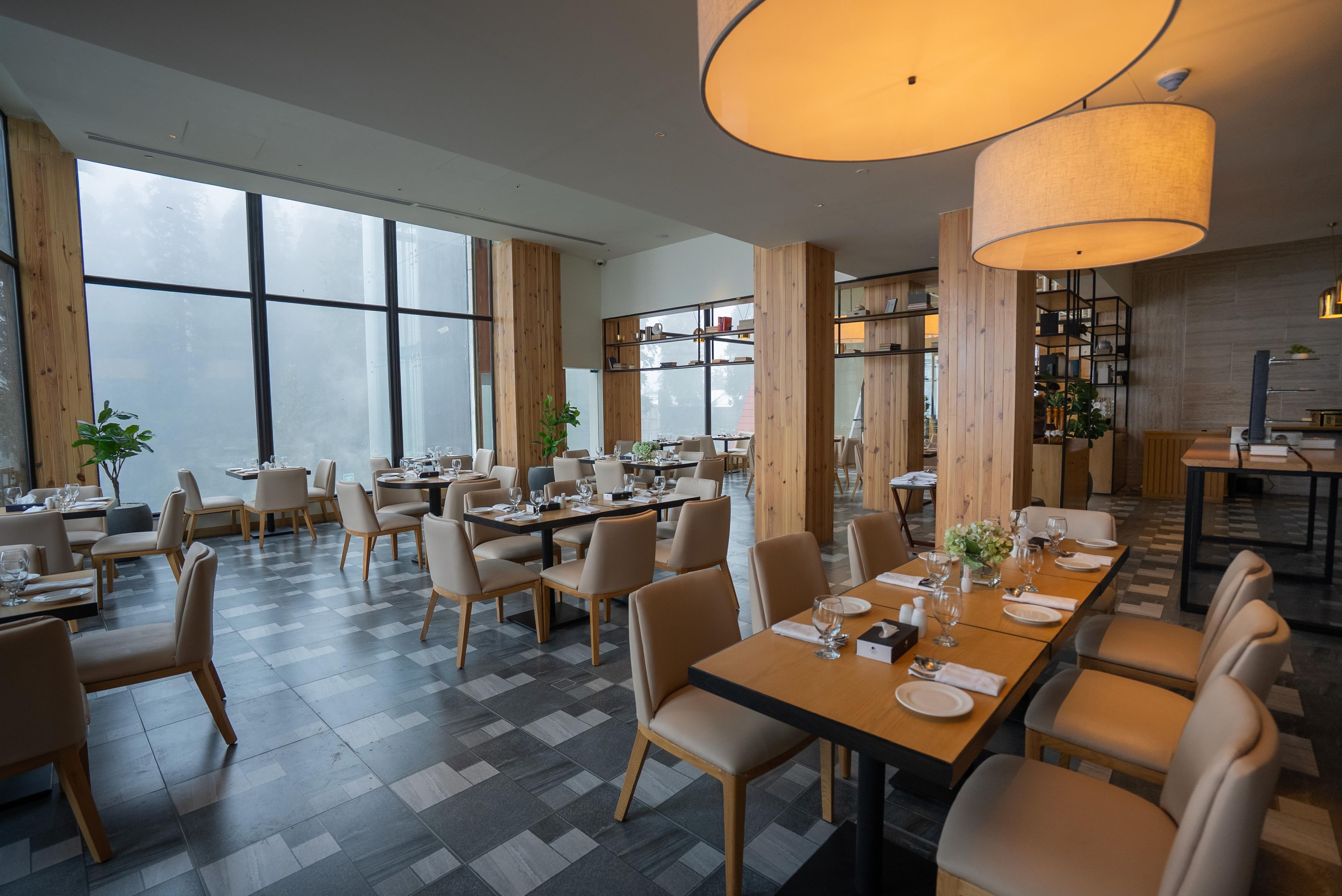 Uma sala de jantar moderna com pé direito alto, grandes janelas e diferentes opções de assento.