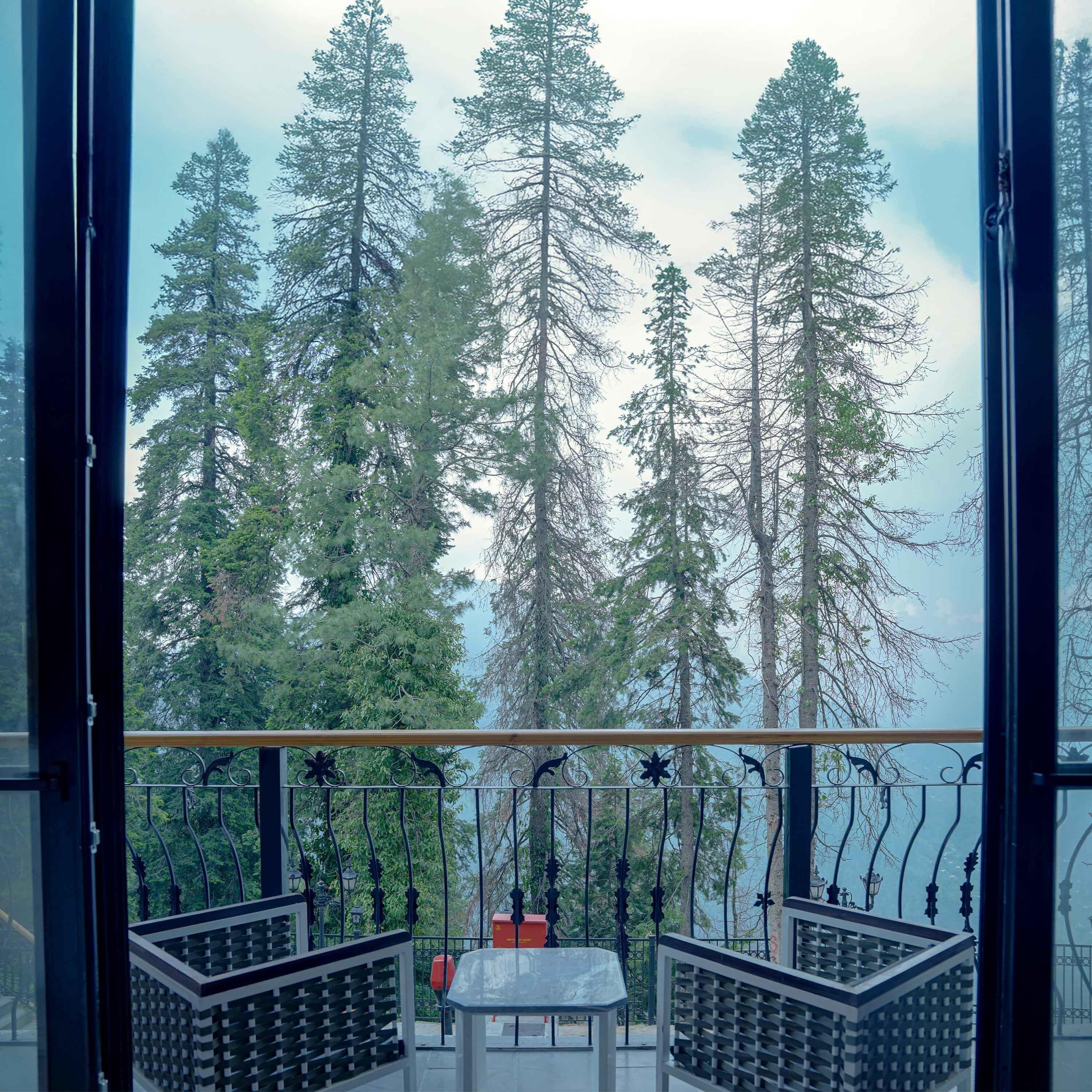A balcony with a view of tall trees and a body of water.