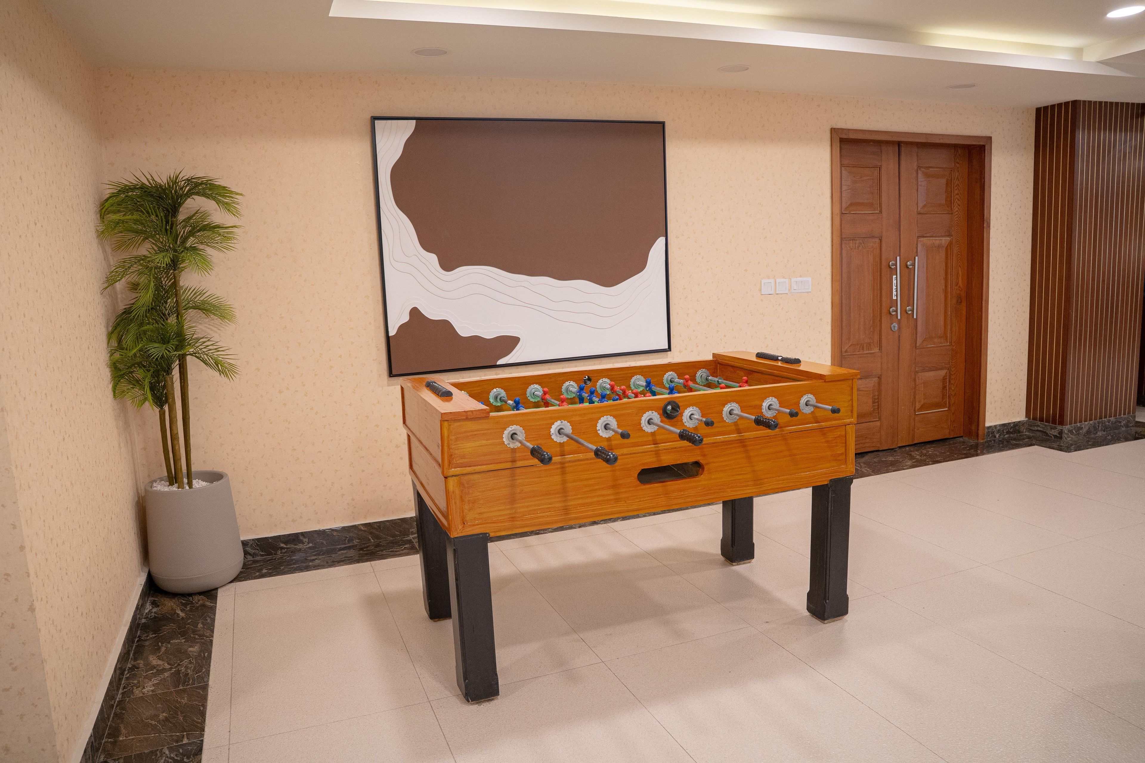 A foosball table in a hotel lobby with a large painting on the wall and a potted plant beside it.