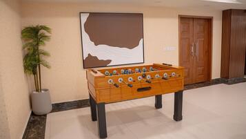 A foosball table in a hotel lobby with a large painting on the wall and a potted plant beside it.
