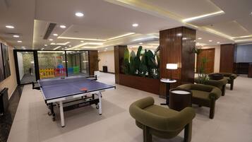A room with a ping pong table, seating area, and a reception desk.
